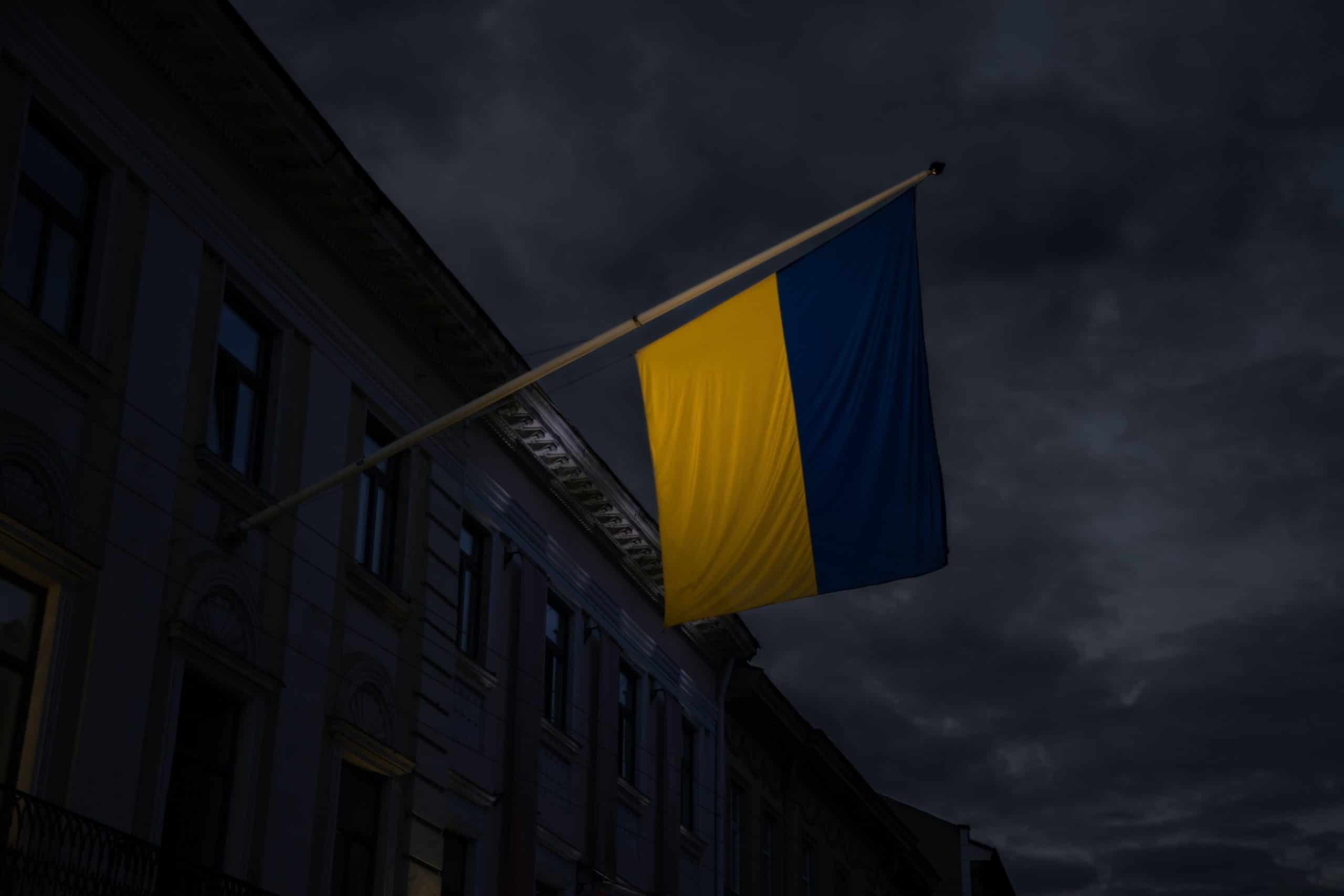 Ukrainian flag flying from side of building, against a dark-set stormy sky