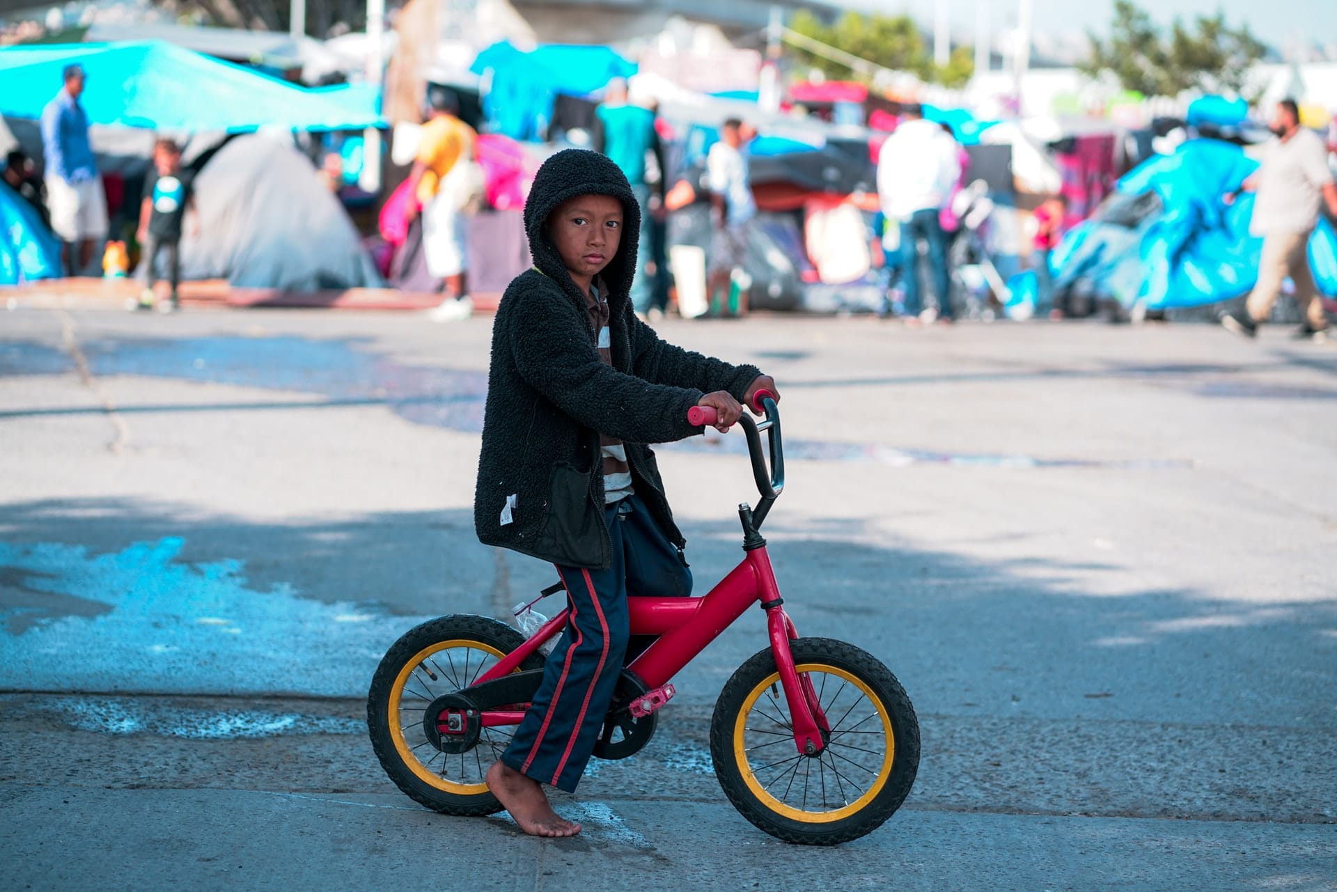 Migrant child in front of displacement tent city, representing humanitarian and compassionate grounds