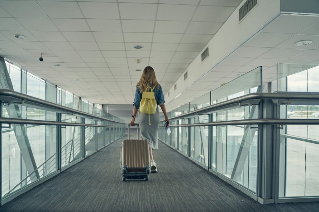 A woman pulls her suitcase on wheels behind her as she makes her way down an airport walkway from the rear with windows on either side of her, representing Canadian Immigration 2026.