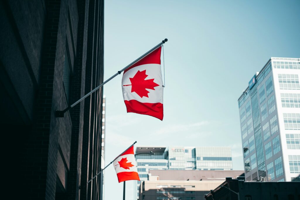 Two Canadian flags mounted on the side of a building with office buildings against a blue sky in the background, representing incomplete immigration applications.